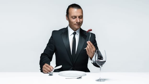 Portrait of a young man in image of maniak with knife, fork and and a piece of raw meat on a plate. Man in suit. The image in the style of Halloween