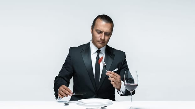 Portrait of a young man in image of maniak with knife, fork and and a piece of raw meat on a plate. Man in suit. The image in the style of Halloween