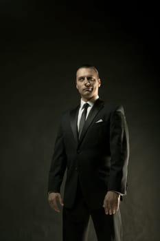 The attractive mature man in black suit on dark studio background
