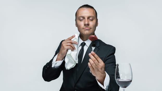 Portrait of a young man in image of maniak with knife, fork and and a piece of raw meat on a plate. Man in suit. The image in the style of Halloween