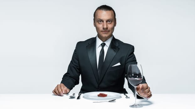Portrait of a young man in image of maniak with knife, fork and and a piece of raw meat on a plate. Man in suit. The image in the style of Halloween