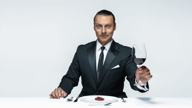 Portrait of a young man in image of maniak with knife, fork and and a piece of raw meat on a plate. Man in suit. The image in the style of Halloween