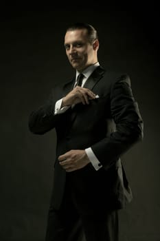 The attractive mature man in black suit on dark studio background