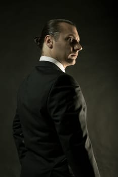 The attractive mature man in black suit on dark studio background