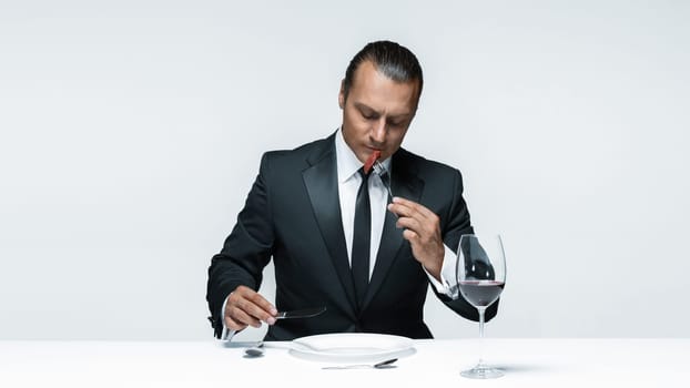 Portrait of a young man in image of maniak with knife, fork and and a piece of raw meat on a plate. Man in suit. The image in the style of Halloween