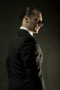 The attractive mature man in black suit on dark studio background