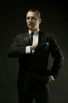 The attractive mature man in black suit on dark studio background