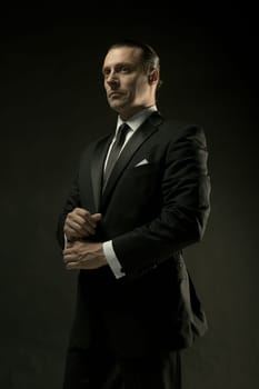 The attractive mature man in black suit on dark studio background