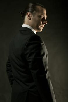 The attractive mature man in black suit on dark studio background