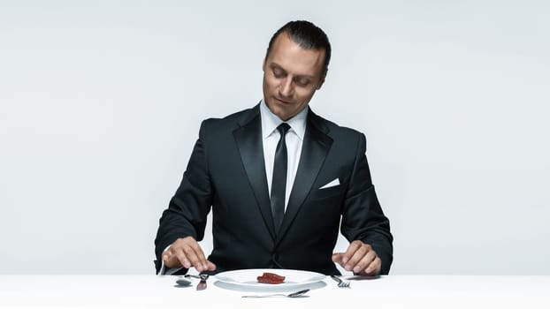 Portrait of a young man in image of maniak with knife, fork and and a piece of raw meat on a plate. Man in suit. The image in the style of Halloween