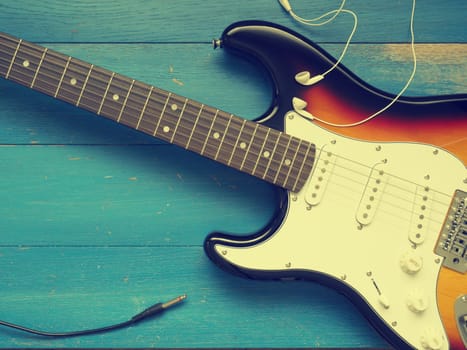 Music concept image, vintage guitar with earphones on a rustic wooden background, Jazz, rock or blues music concept