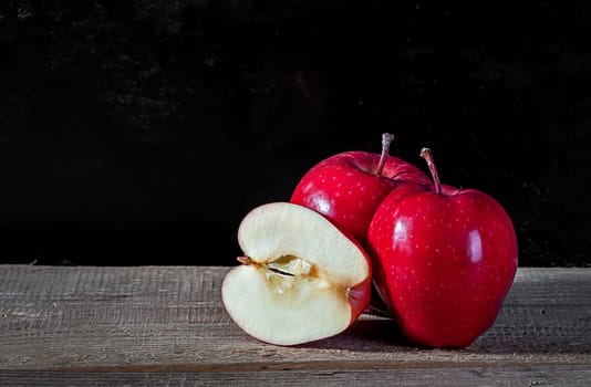Whole and cut in half apple lying on textured wooden table on dark background
