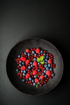 Mix of fresh berries in a bowl on black background