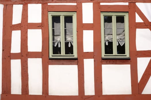 The beam construction and the wooden scaffolding of a half-timbered house with two narrow wooden windows.