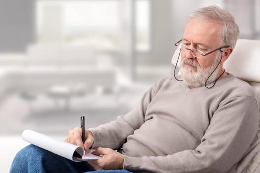 Old man making a shopping list with a pen on paper for holidays