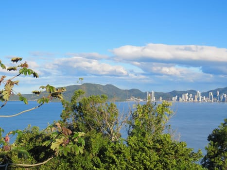Coastal city landscape with forest in the foreground, late afternoon in blue sea