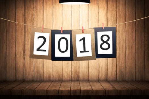 2018 number on paperboard for New Year hanging on rope with wooden background