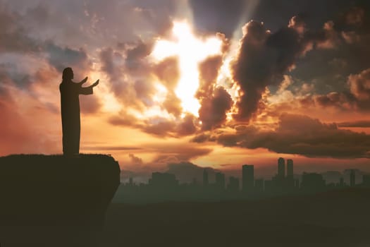 Silhouette of man praying to god with ray of light shaping cross on the sky