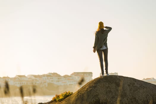 Beautiful woman with yellow cap over the cliff seeing the beach