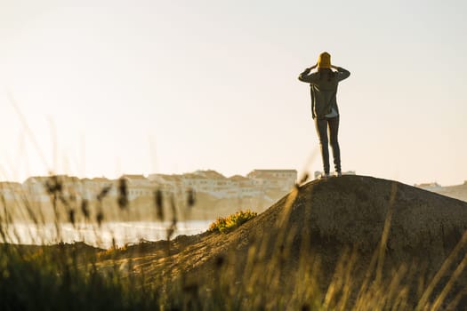 Beautiful woman with yellow cap over the cliff seeing the beach