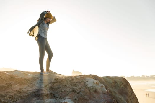 Beautiful woman with yellow cap over the cliff seeing the beach