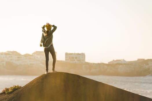 Beautiful woman with yellow cap over the cliff seeing the beach