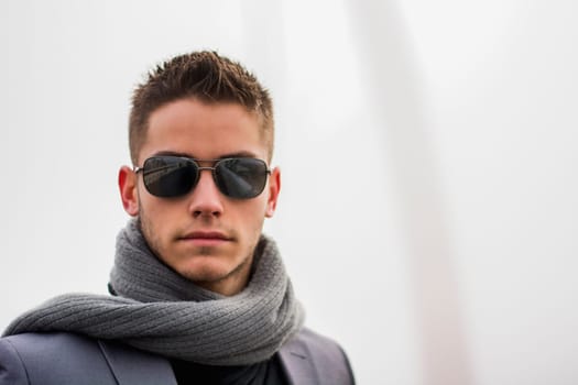 Headshot of attractive young man outdoor wearing sunglasses and scarf on elegant jacket