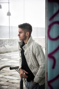 Handsome young man outdoor in city setting, wearing winter clothes, side view