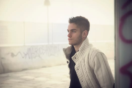 Handsome young man outdoor in city setting, wearing winter clothes, side view