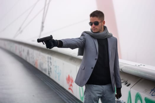 Well dressed handsome young detective or policeman or mobster standing in an urban environment aiming a gun to left side