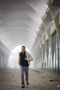 Front View of Young Man Running Through Abandoned Arched Tunnel Towards Camera
