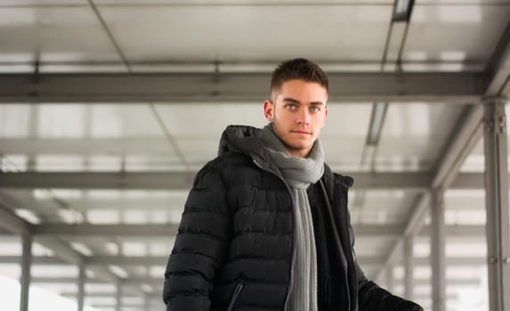 Attractive young man under tunnel in urban environment, looking at camera, wearing winter clothing