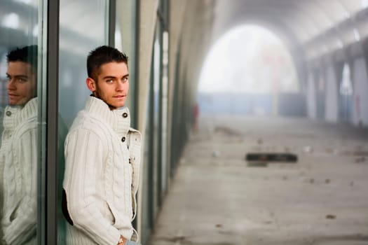 Attractive young man in abandoned empty tunnel, leaning against shop window