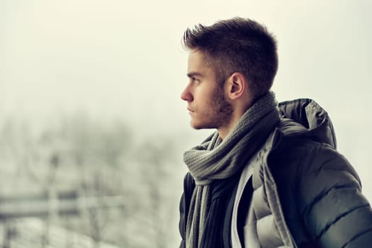Profile view of handsome young man outdoor in winter wearing scarf, looking away thinking