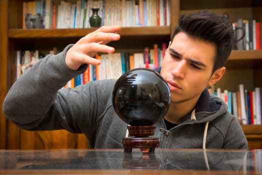 Handsome young male soothsayer predicting the future by looking into black crystal ball