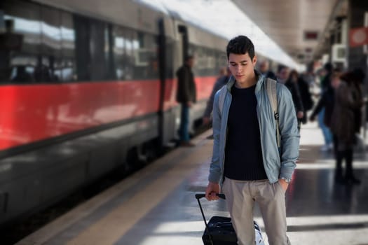 Handsome young male traveler in train station with trolley suitcase, looking down