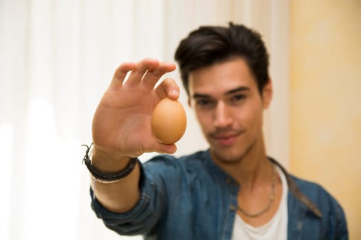 Smiling young man holding an egg in his hand, showing it to the camera