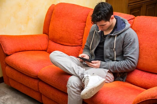 Handsome young man at home reading with ebook reader sitting on a couch