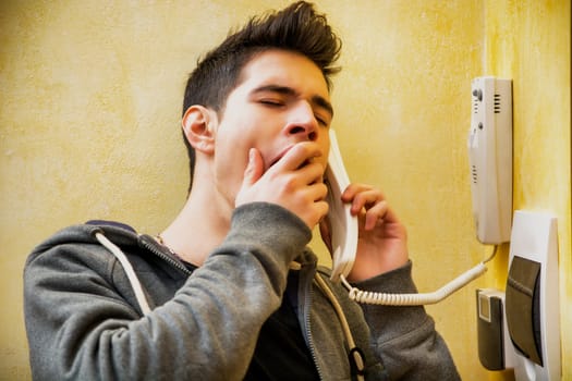 Young man or teenager answering the intercom at the entrance in an apartment yawning
