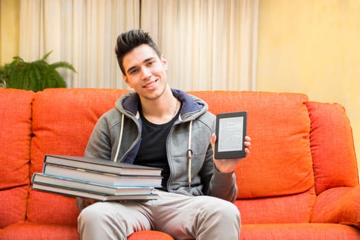 Smiling young man showing difference between light and handy ebook reader in one hand and heavy books on other hand