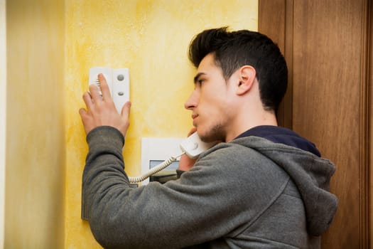 Teenager or young man answering the intercom in an apartment, pressing button to open entrance door