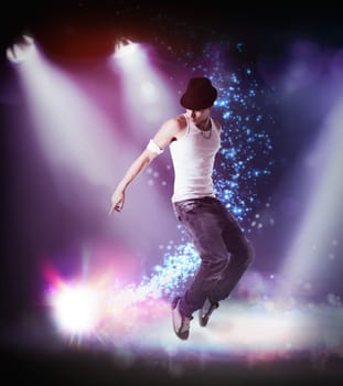 Trendy young man in hat hip hop dancing, breakdancing on a stage, in the beams of three spotlights leaping in the air with bent knees