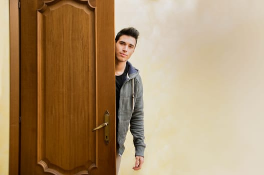 Handsome young man behind open door, getting out, looking at camera with friendly expression