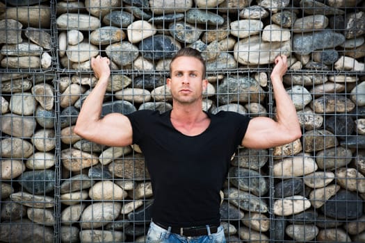 Muscular sexy man in front of stone wall, showing bulging biceps