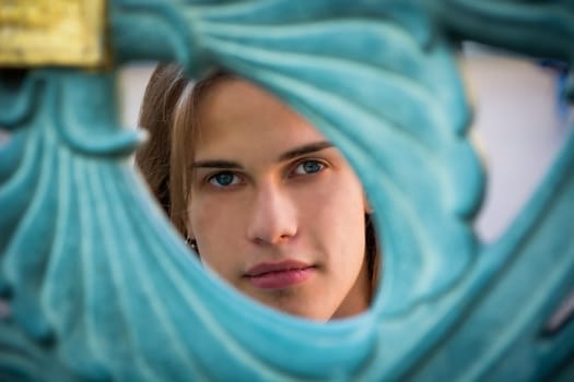 Gorgeous Long Hair Man Peeking Through Hole behind Blue Green Art Metal Gate