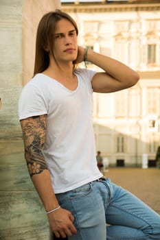 Handsome Long Hair Man on White Shirt Standing in Square in Turin city Center, Italy, with Old Palace Behind Him