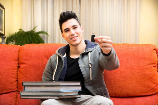 Smiling young man showing difference between light and handy USB key in one hand and heavy books on other hand