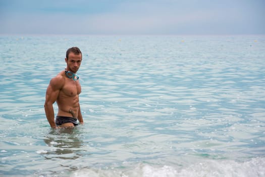 Handsome muscular young man at the beach standing in the sea in profile pose