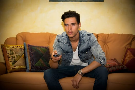 Young man sitting watching television changing the channel with the remote control