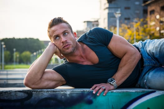 Handsome muscular blond man lying down in city setting looking to a side